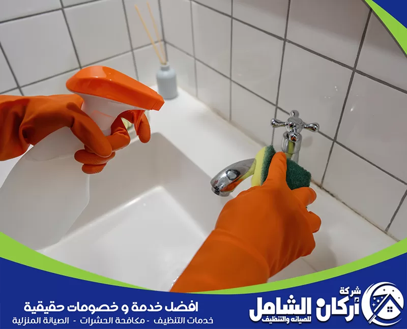 رائحة المجاري في الحمام 0500073610 أركان الشامل شخص يرتدي قفاز برتقالي يقوم بتنظيف حوض غسيل في الحمام.