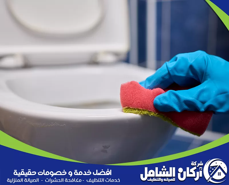 علاج تسربات خفية حول الحوض 0500073610 أركان الشامل شخص يرتدي قفازات زرقاء يقوم بتنظيف مرحاض، مع التركيز على إزالة الروائح الكريهة.